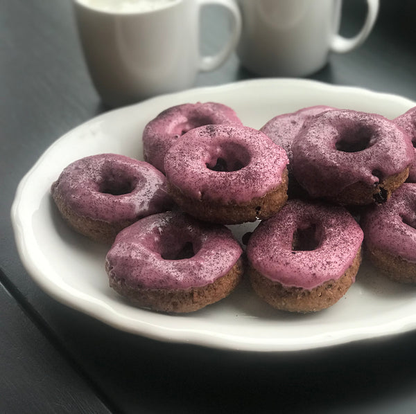 Blueberry glazed doughnuts on white platter in front of two white mugs