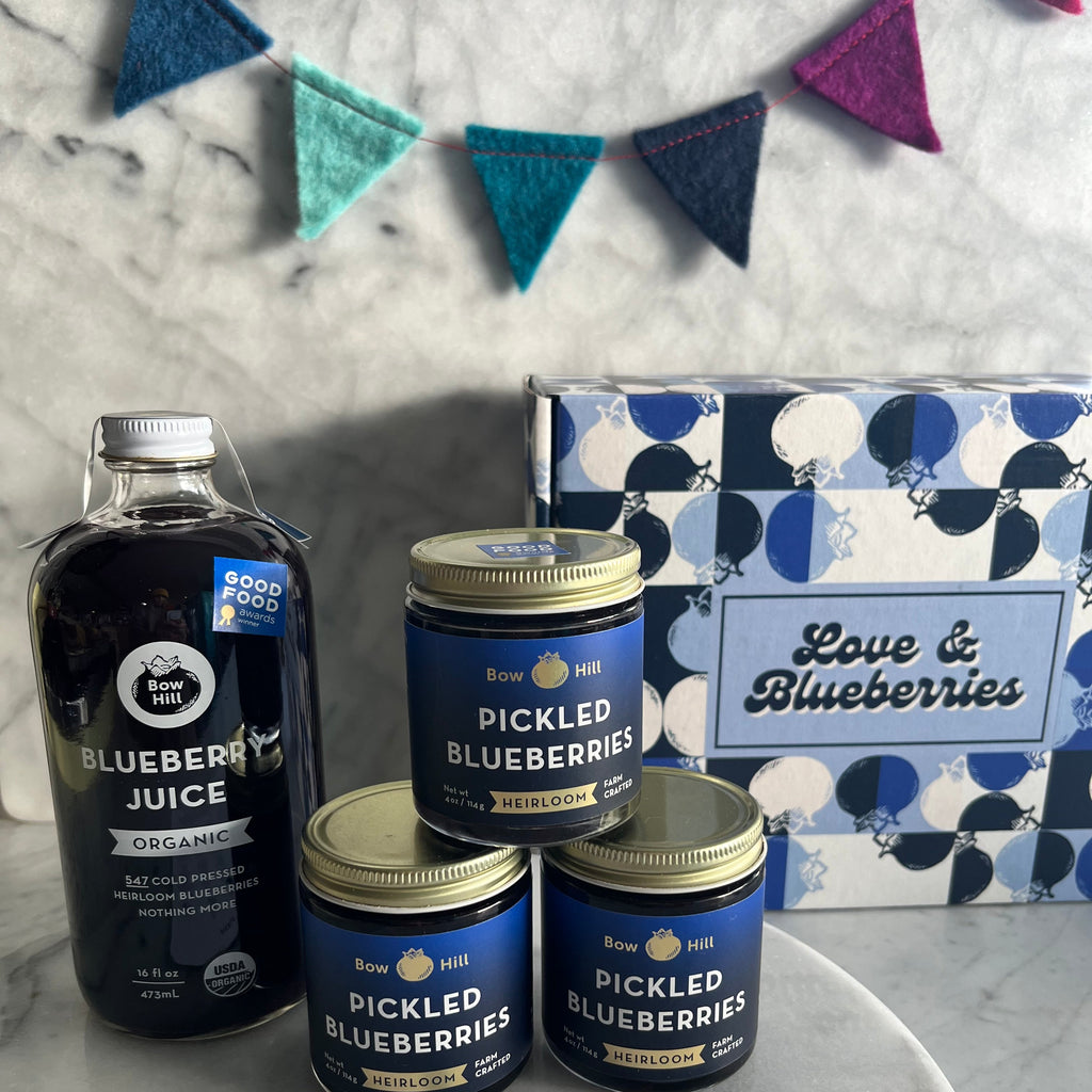 Pickled blueberries and blueberry juice on a marble surface with decorative elements.